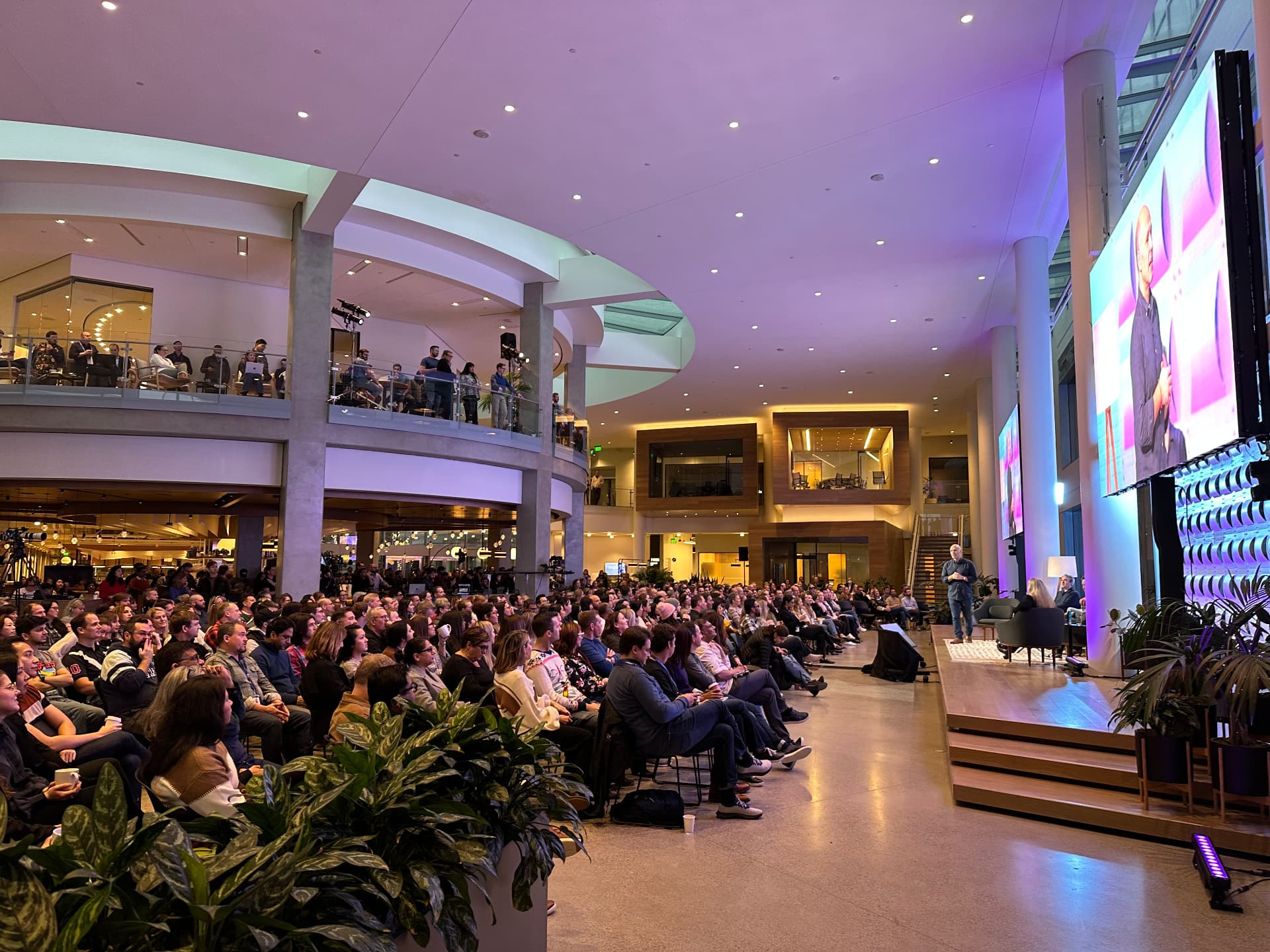 A packed atrium town hall with a speaker on stage